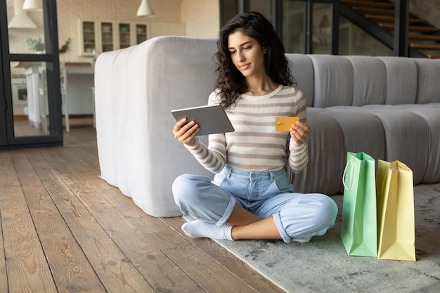 Foto jovem alegre com sacolas de compras fazendo pagamento remoto usando tablet e cartão de crédito encomendando mercadorias na loja da web