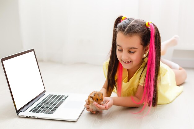 Jovem alegre com um hamster de estimação usando o computador portátil, estudando através do sistema de e-learning online em casa. Aprendizagem à distância ou à distância