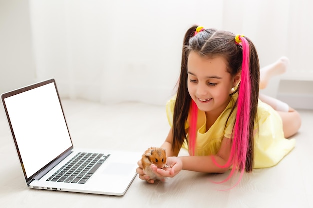 Jovem alegre com um hamster de estimação usando o computador portátil, estudando através do sistema de e-learning online em casa. Aprendizagem à distância ou à distância