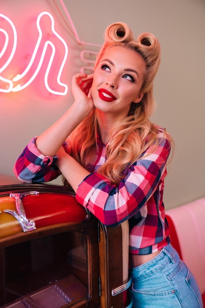 Foto jovem alegre com um lindo penteado sorrindo enquanto se inclina para uma jukebox em um café americano retrô