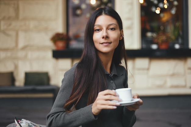 Foto jovem alegre com uma xícara de café sentada em um café sorrindo ao ar livre
