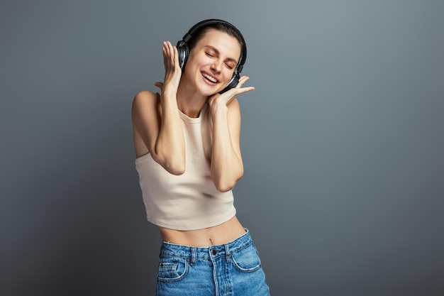 Jovem alegre curtindo música com fone de ouvido usando top casual isolado em fundo cinza