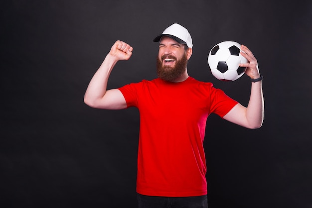 Jovem alegre de camiseta vermelha segurando uma bola de futebol e comemorar a vitória