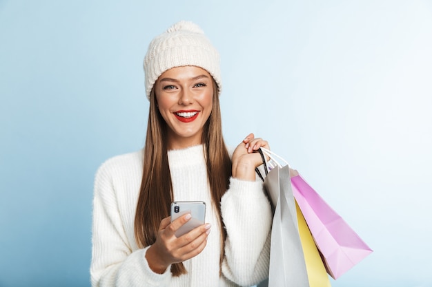 Jovem alegre de suéter, segurando um celular, carregando sacolas de compras