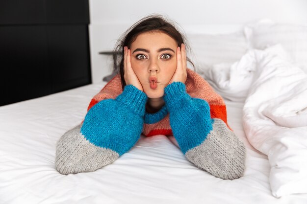 Foto jovem alegre deitada na cama em casa, se divertindo