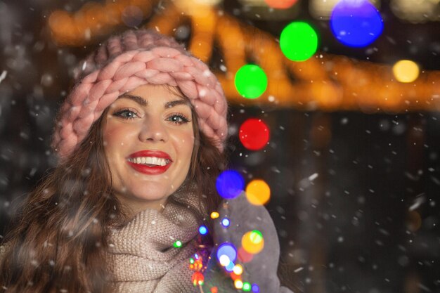 Jovem alegre desfrutando de neve posando com guirlandas na cidade. Espaço vazio