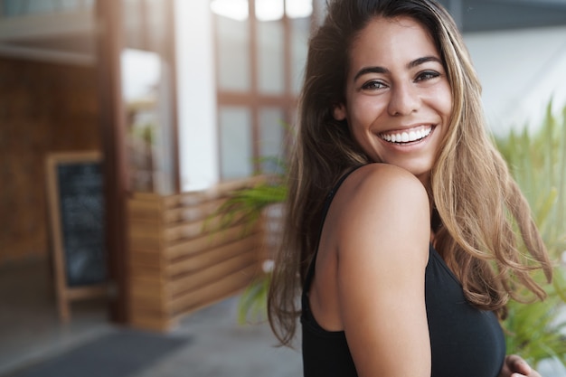 Foto jovem alegre e bonita, bronzeada, inclinada no terraço e olhando feliz