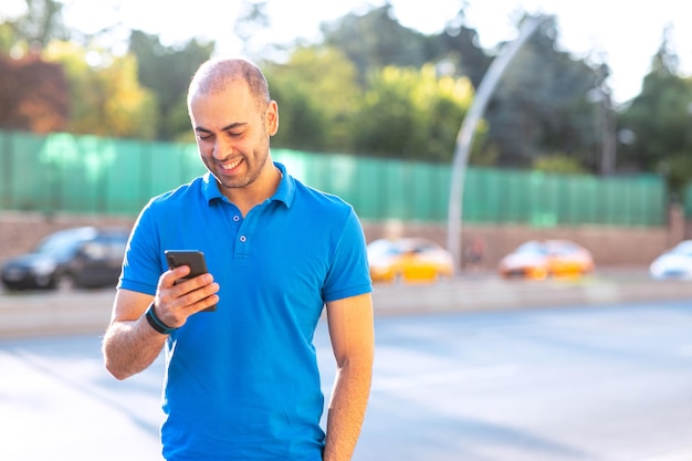 Jovem alegre e confiante verificando seus e-mails e olhando para seu telefone inteligente em um espaço urbano Inclui cópia e texto