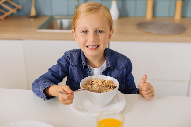 Foto jovem alegre e positiva sorrindo e mostrando o polegar para cima enquanto toma um café da manhã saudável e saboroso