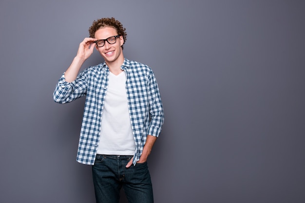 Jovem alegre elegante com uma camisa xadrez casual tocando os óculos