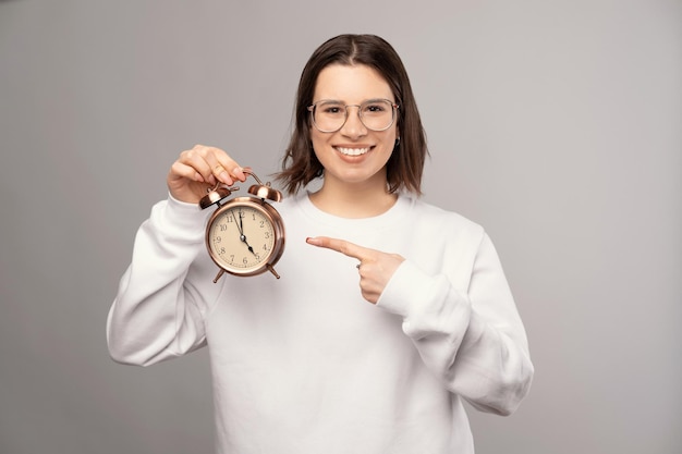 Jovem alegre está apontando para o despertador que ela está segurando