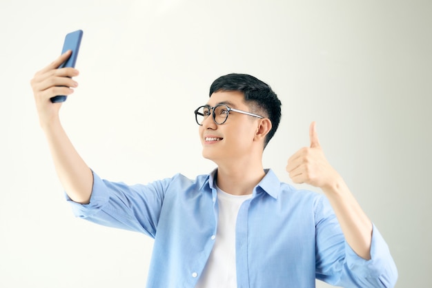 Jovem alegre fazendo selfie com seu telefone e mostrando o polegar