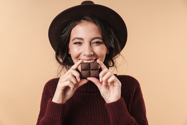 Foto jovem alegre feliz linda mulher isolada sobre a parede bege segurando chocolate.