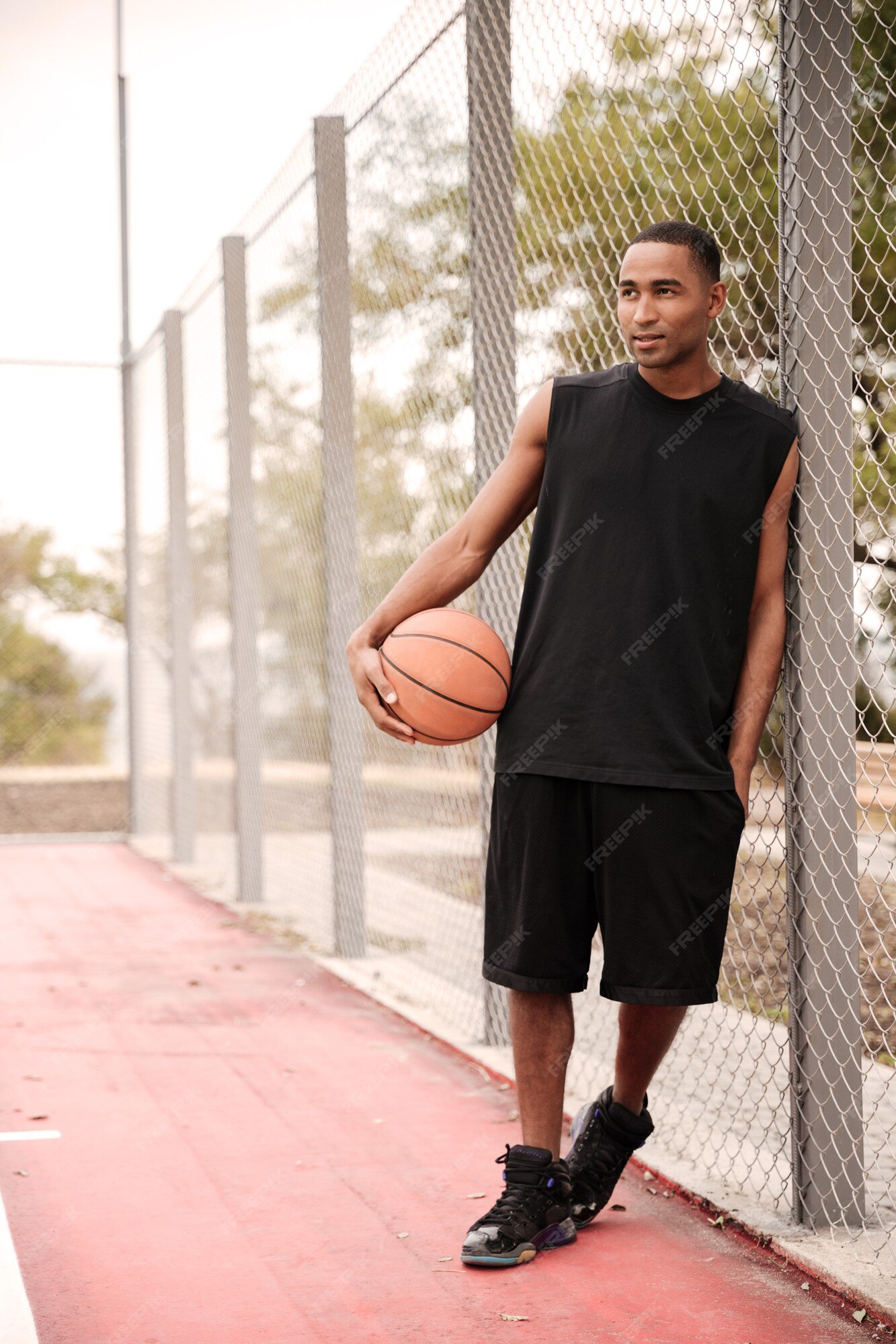 Jovem jogador de basquete feliz sentado no parque com uma toalha