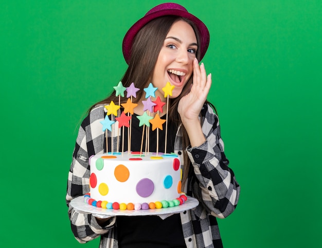 Jovem alegre linda com um chapéu de festa segurando um bolo e ligando para alguém