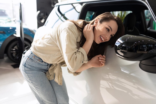 Foto jovem alegre olha no espelho lateral de um carro em uma concessionária de carros