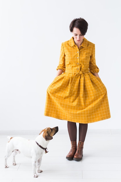 Jovem alegre posando em um vestido amarelo com seu amado cachorro Jack Russell Terrier de pé em uma parede branca