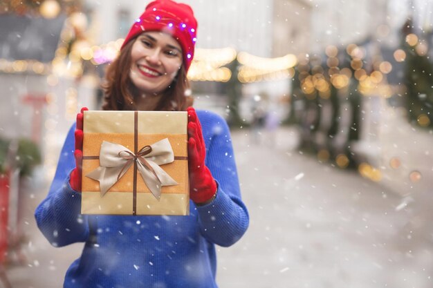 Jovem alegre recebendo um presente na feira de inverno do feriado durante a queda de neve. Espaço para texto