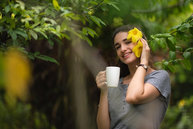 Jovem alegre relaxando e respirando ar fresco enquanto está sentado na varanda com vista para a natureza e bebendo café da manhã e bebidas