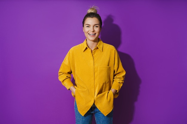 Jovem alegre rindo vestindo camisa amarela contra fundo roxo