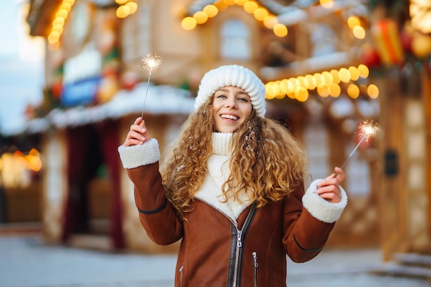 Jovem alegre segurando um faísca na mão na rua de inverno luzes de guirlandas festivas