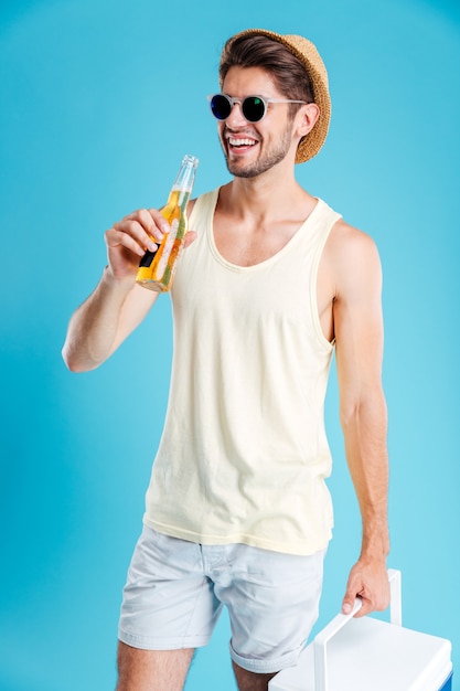 Jovem alegre segurando uma bolsa térmica e bebendo cerveja