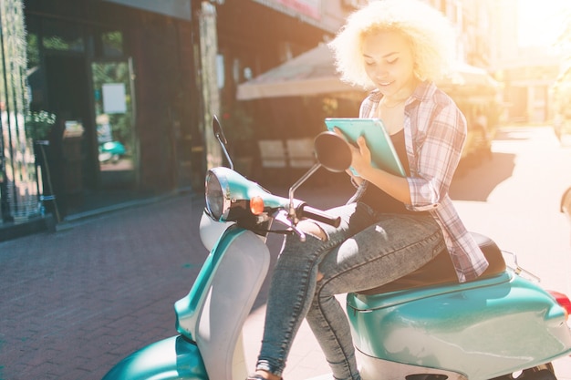 Jovem alegre sentada na scooter e usando o tablet digital