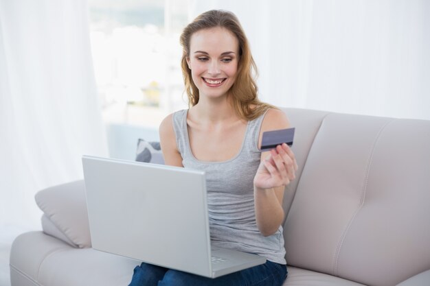Jovem alegre sentada no sofá usando laptop para compras on-line