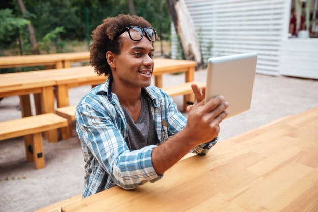 Jovem alegre sentado e usando o tablet ao ar livre