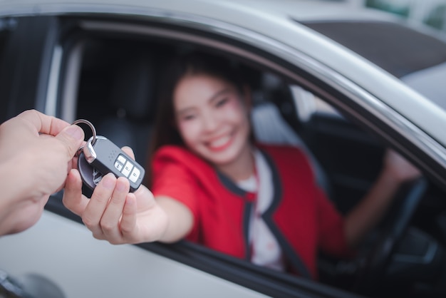 Jovem alegre, sentado em um carro com as chaves na mão - conceito alugar um carro