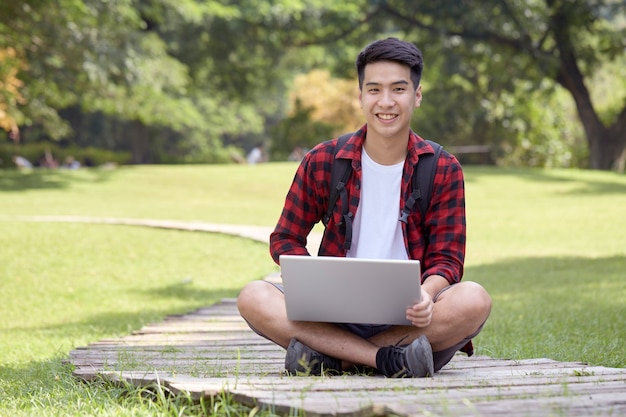 Jovem alegre sentado no parque usando um laptop