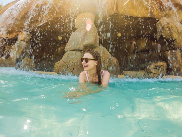 Foto jovem alegre sob as fontes termais do spa do dia da piscina do córrego da água