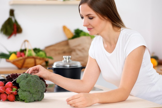 Jovem alegre sorridente está pronta para cozinhar em uma cozinha Dona de casa sentada à mesa e olhando para a câmera