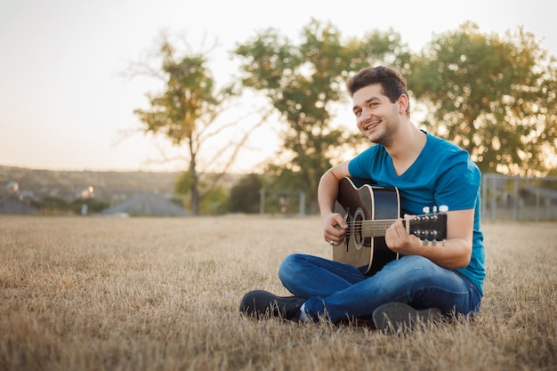 Jovem alegre tocando violão lá fora. Músico de vibração positiva.