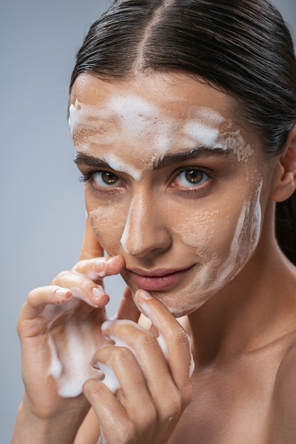 Jovem alegre usando espuma para tratamento facial