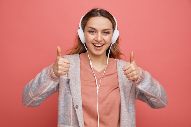 Jovem alegre usando fones de ouvido mostrando o polegar para cima