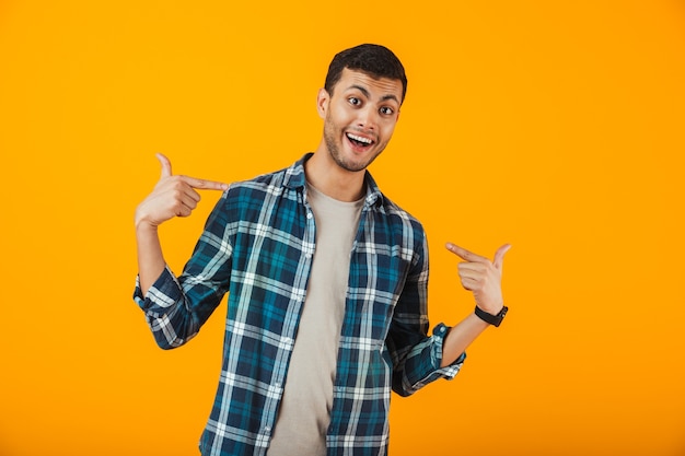 Jovem alegre vestindo uma camisa xadrez em pé isolado na parede laranja, apontando o dedo para si mesmo