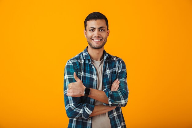 Jovem alegre vestindo uma camisa xadrez em pé, isolado na parede laranja, com os braços cruzados