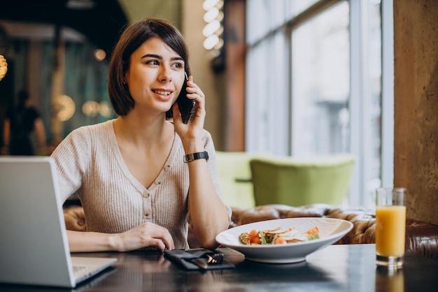 Jovem almoçando em um café e trabalhando no laptop