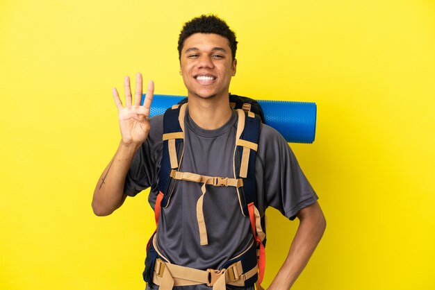 Jovem alpinista afro-americano com uma grande mochila isolada em um fundo amarelo feliz e contando quatro com os dedos