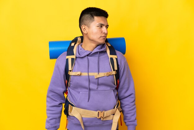 Jovem alpinista com uma grande mochila isolada em um fundo amarelo, olhando para o lado