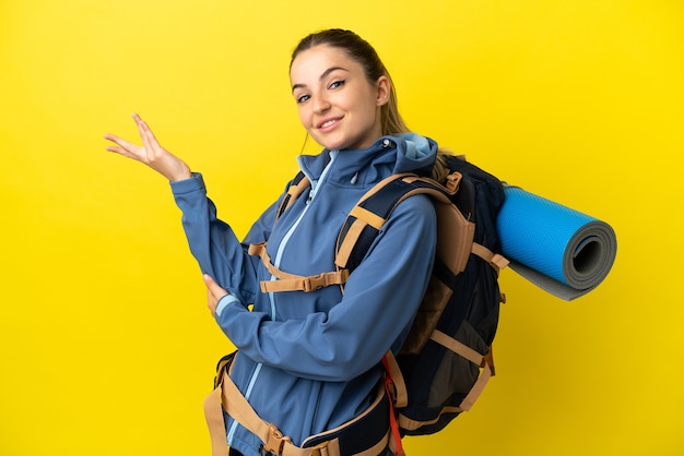 Jovem alpinista com uma grande mochila sobre fundo amarelo isolado