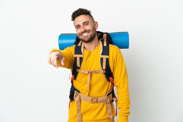 Jovem alpinista com uma grande mochila sobre um fundo isolado apontando para a frente com uma expressão feliz