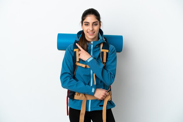 Jovem alpinista com uma grande mochila sobre um fundo isolado apontando para o lado para apresentar um produto