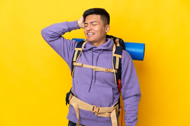 Jovem alpinista com uma mochila grande isolada em um fundo amarelo e sorrindo muito