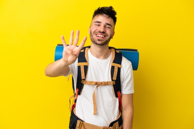 Jovem alpinista homem caucasiano com uma grande mochila isolada em um fundo amarelo feliz e contando quatro com os dedos