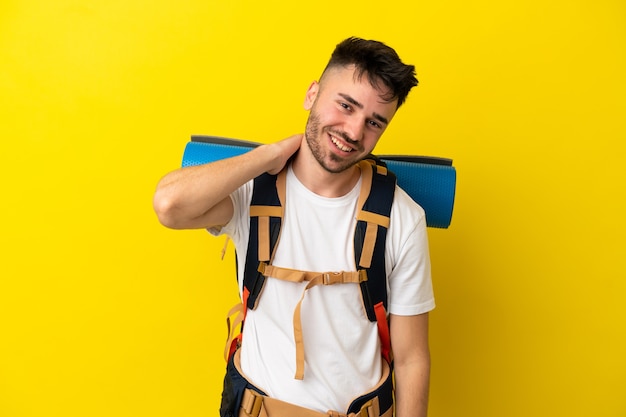 Jovem alpinista homem caucasiano com uma grande mochila isolada em um fundo amarelo rindo