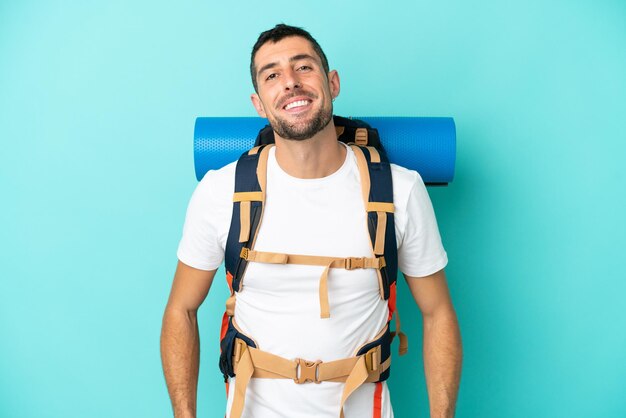 Jovem alpinista homem caucasiano com uma grande mochila isolada em um fundo azul rindo