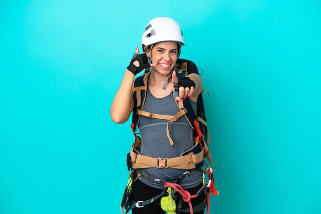 Jovem alpinista italiana isolada em fundo azul, fazendo gesto de telefone e apontando para a frente