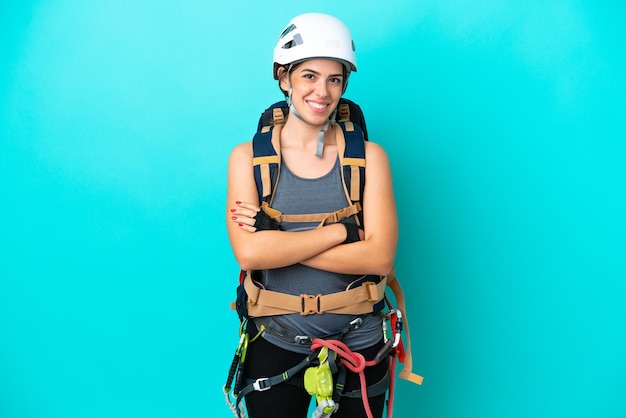 Jovem alpinista italiana isolada em fundo azul, mantendo os braços cruzados em posição frontal